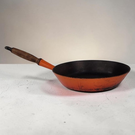 Vintage Le Creuset No. 28 Flame Orange cast iron frying pan with wooden handle.
