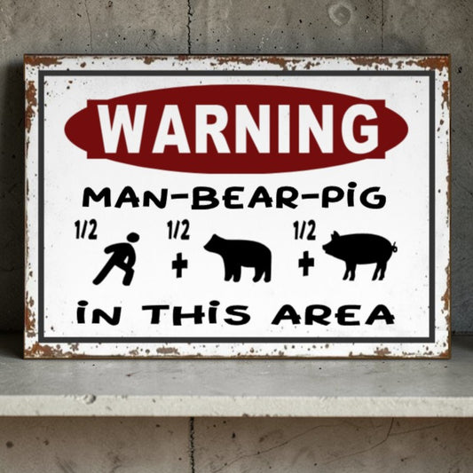 Vintage-style metal sign with humorous 'Warning: Man-Bear-Pig' text on a concrete surface.