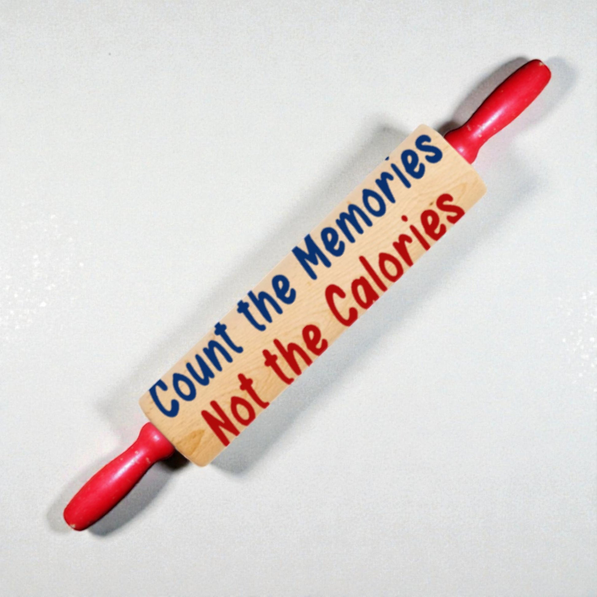 Red rolling pin with wooden plaque reading 'Count the Memories Not the Calories' on a white background