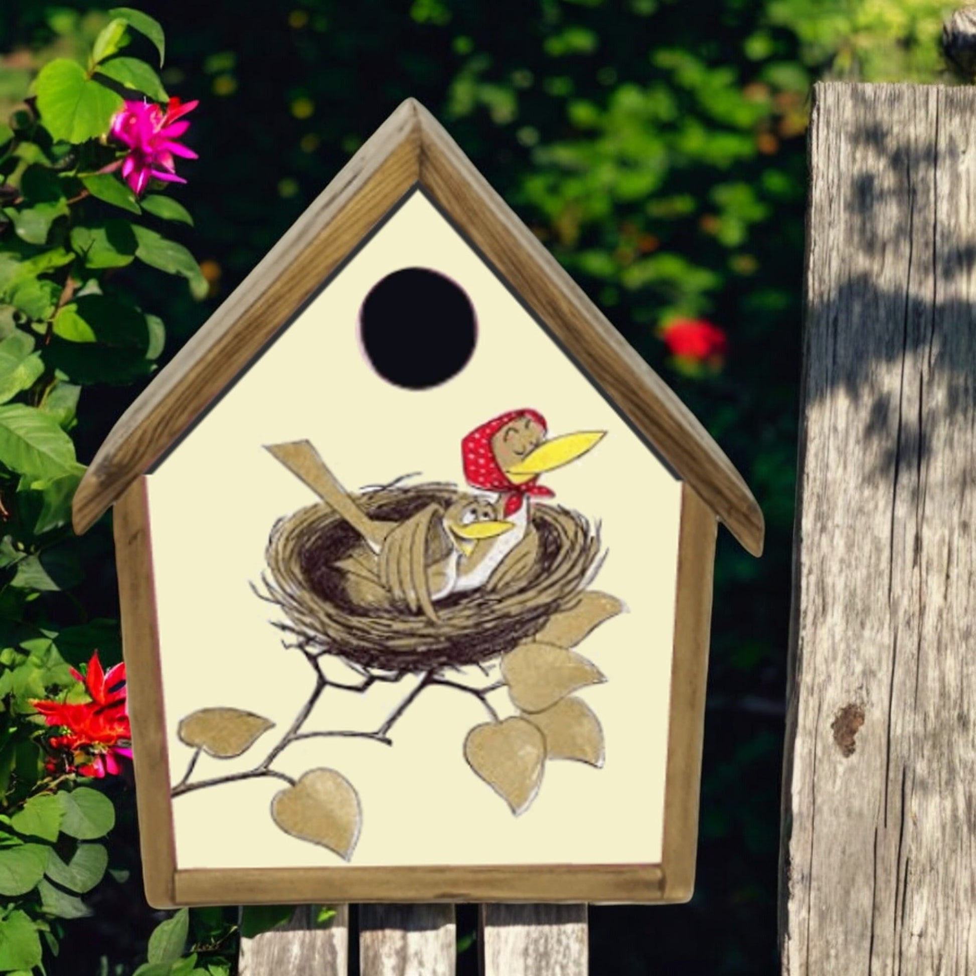 Decorative birdhouse with a design of birds in a nest on a wooden post with flowers in the background.