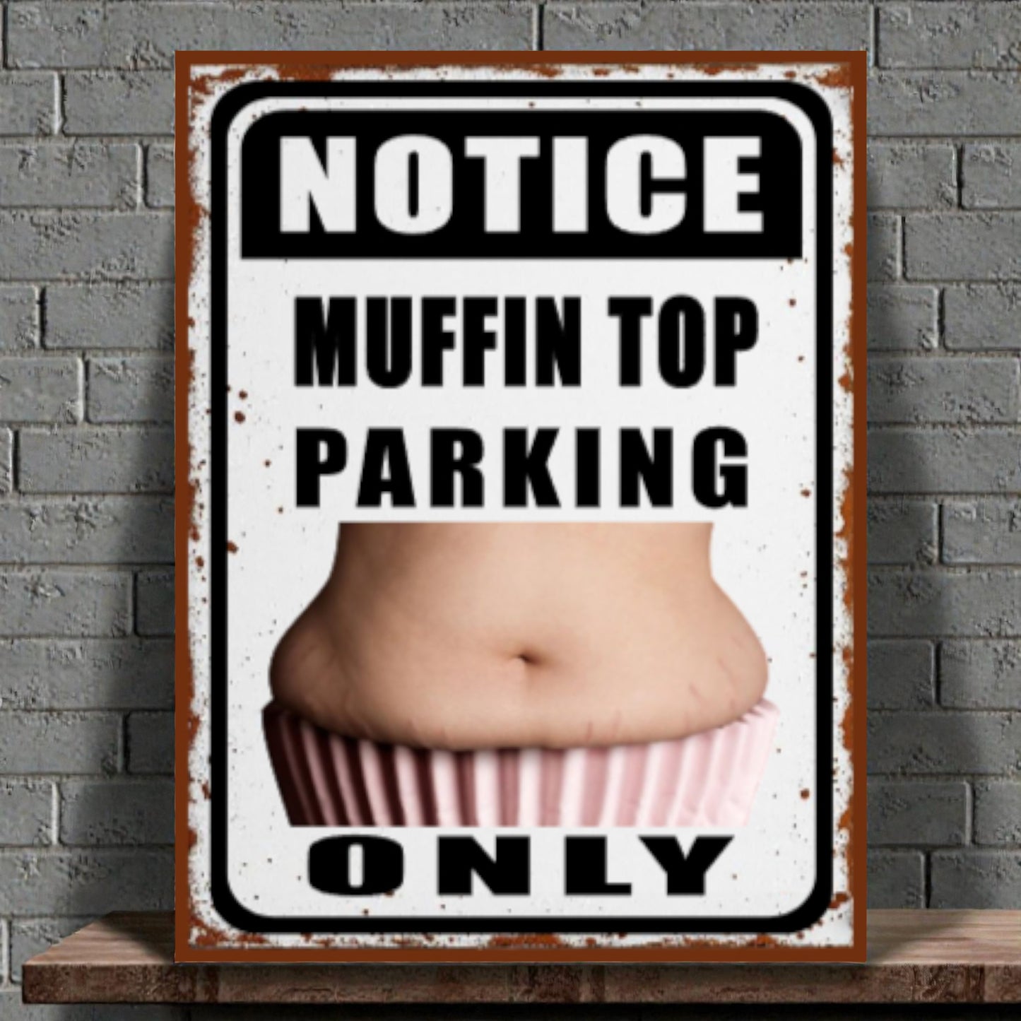 Metal sign with a graphic of a muffin top and text 'Notice Muffin Top Parking Only' on a brick wall background.