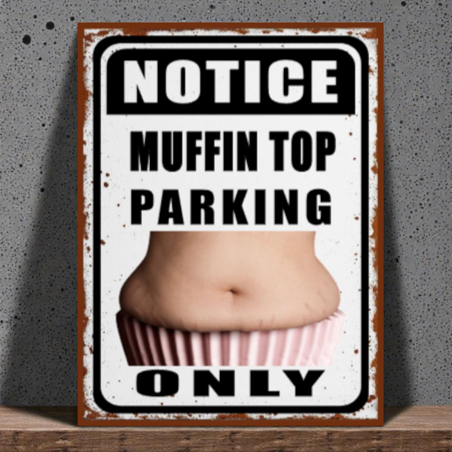 Metal sign with a graphic of a muffin top and text 'Notice Muffin Top Parking Only' on a textured wall background.