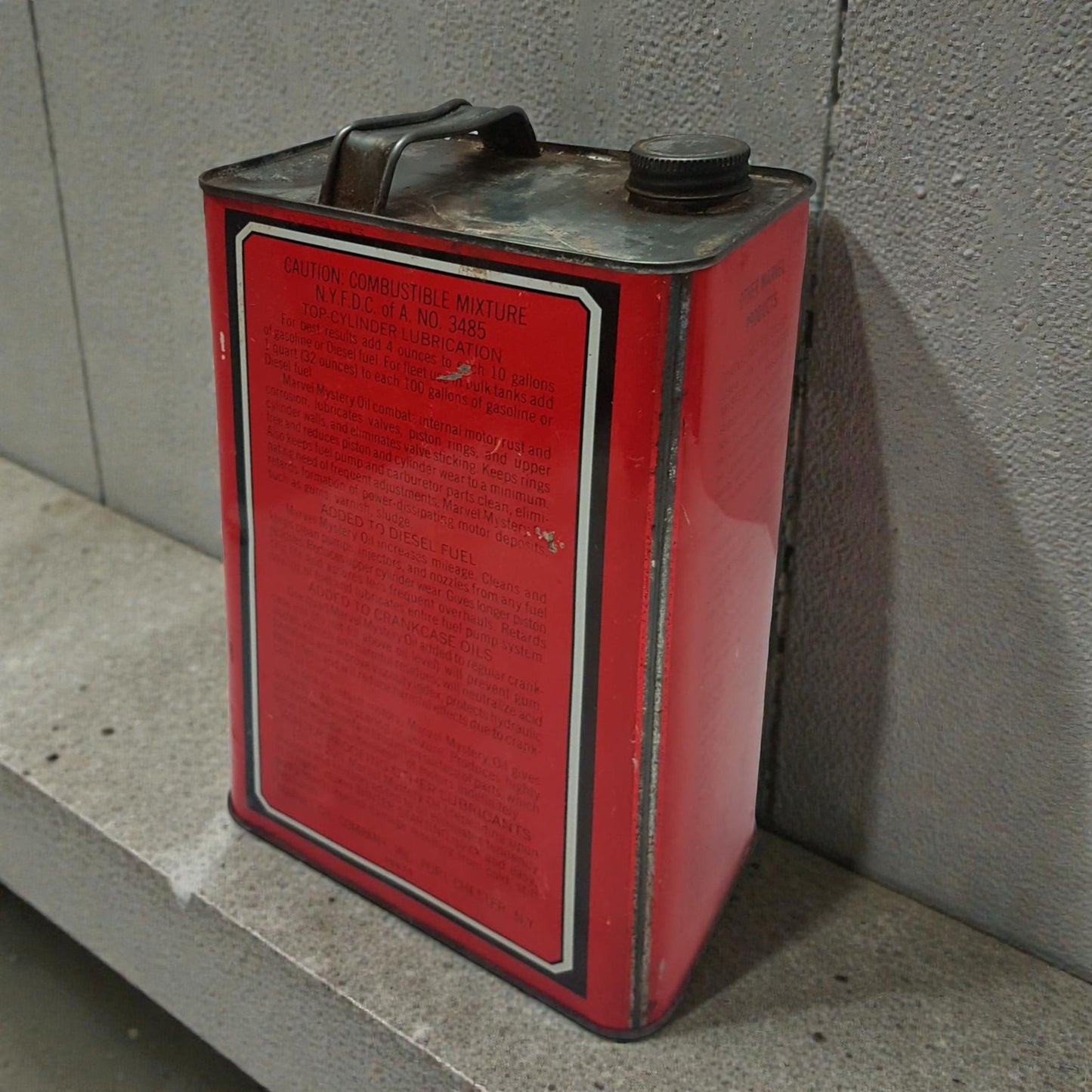 Red metal can with a warning label against a gray wall.