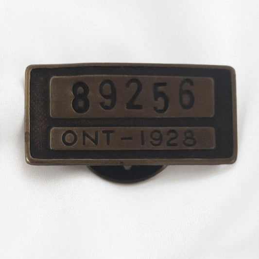 Bronze tag with numbers '89256' and 'ONT-1928' on a white background