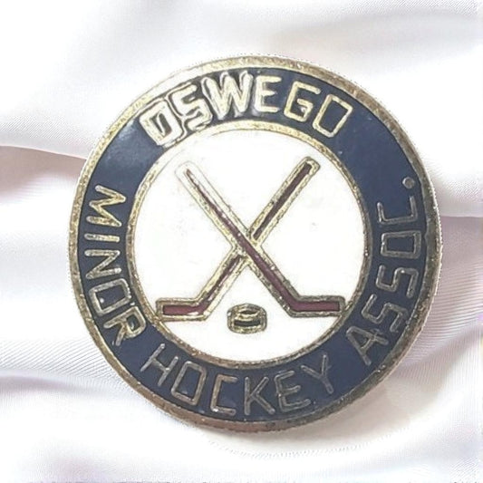 Pin with 'Oswego Minor Hockey Assoc.' text and hockey stick and puck design on a white background
