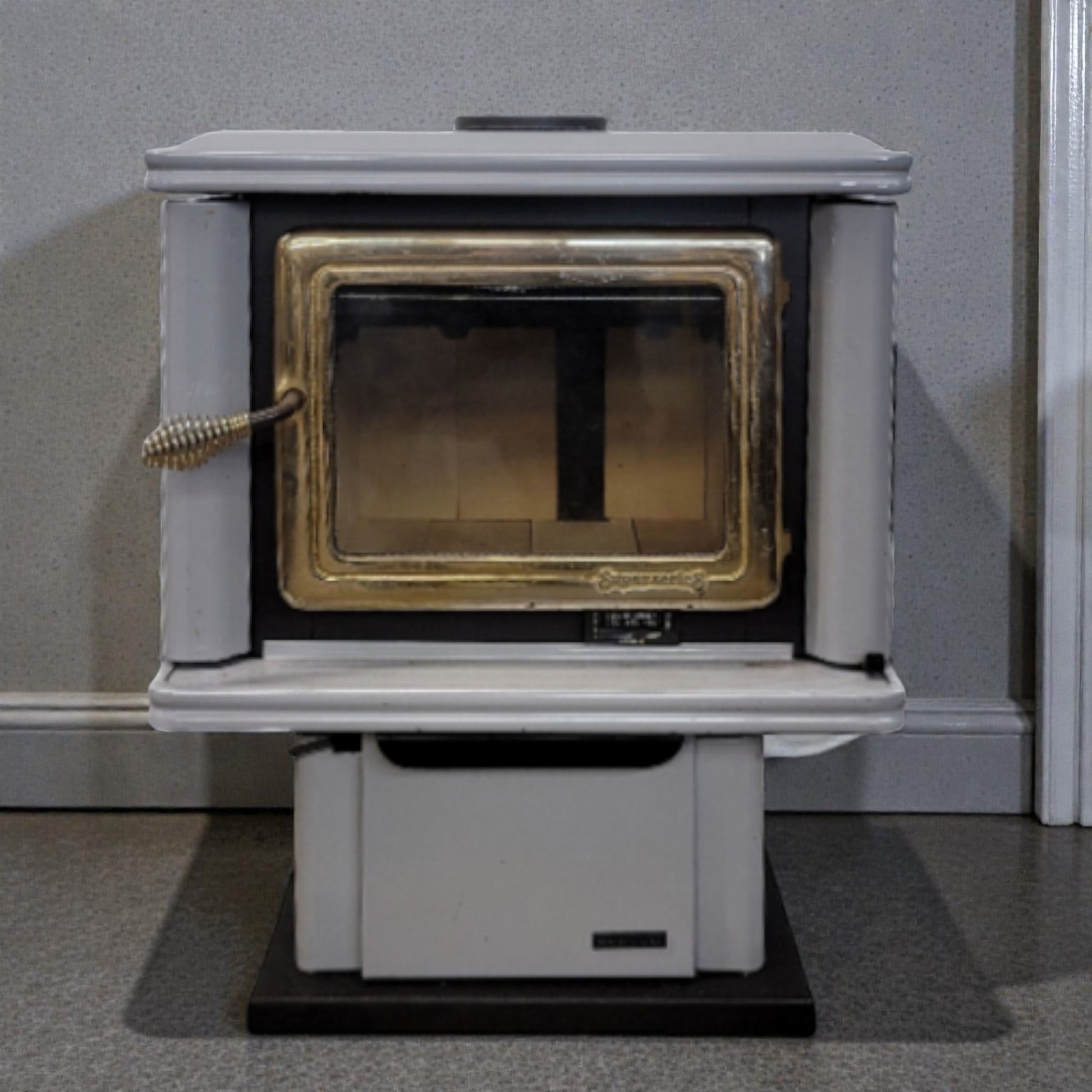 White wood-burning stove with gold interior on a gray floor against a gray wall.
