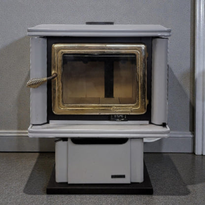 White wood-burning stove with gold interior on a gray floor against a gray wall.