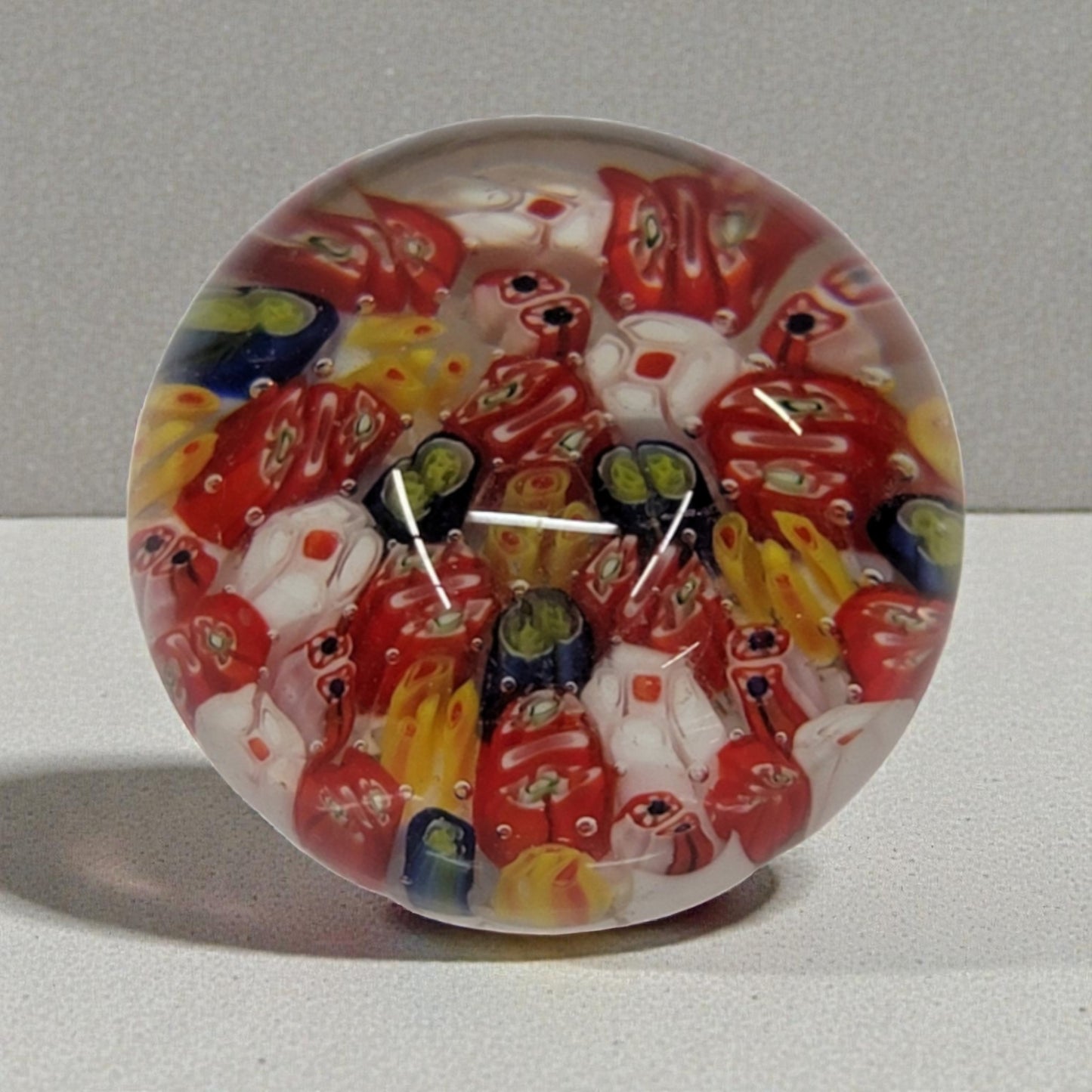 Colorful glass paperweight with red and yellow patterns on a gray background