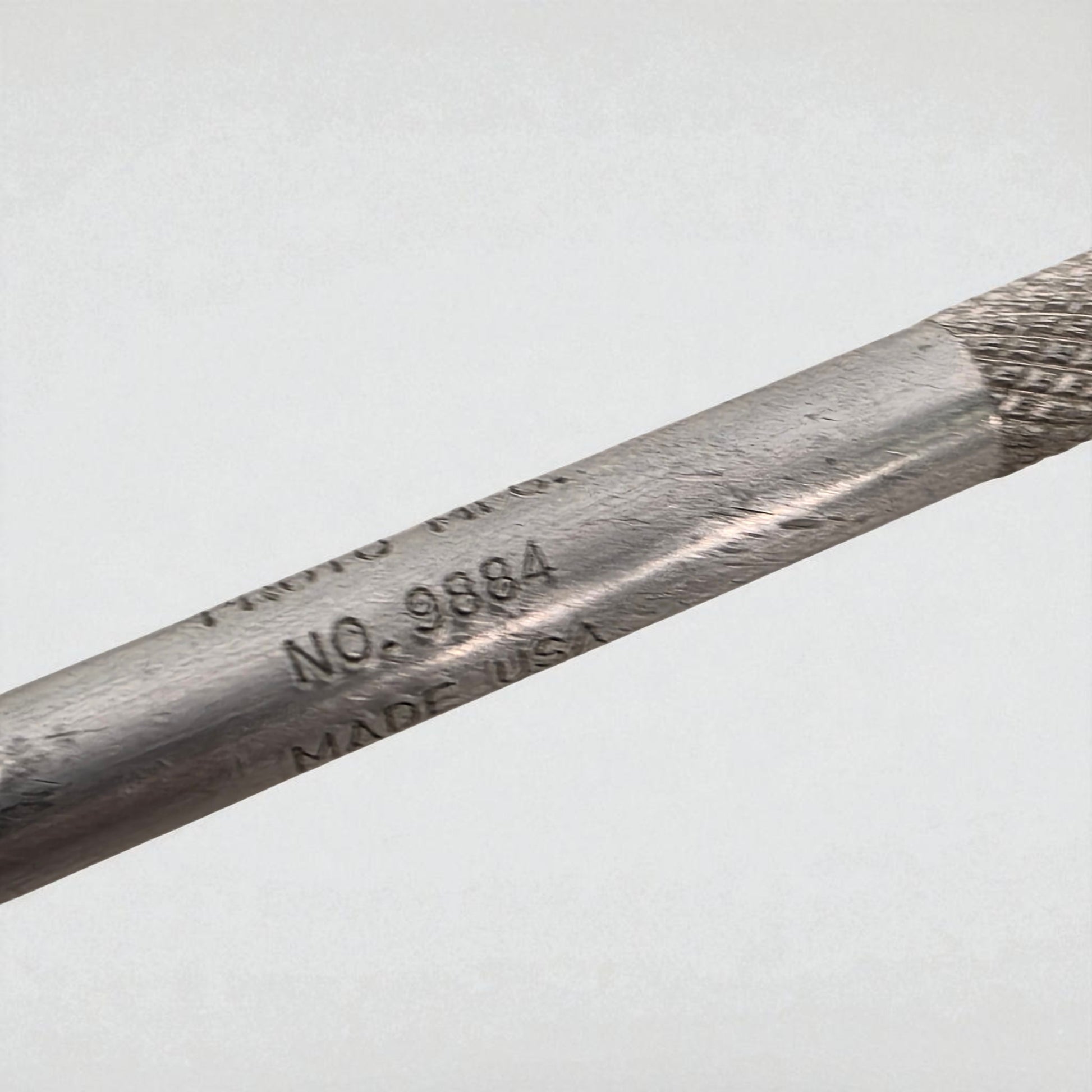Close-up of a metal tool with engraved text on a light gray background