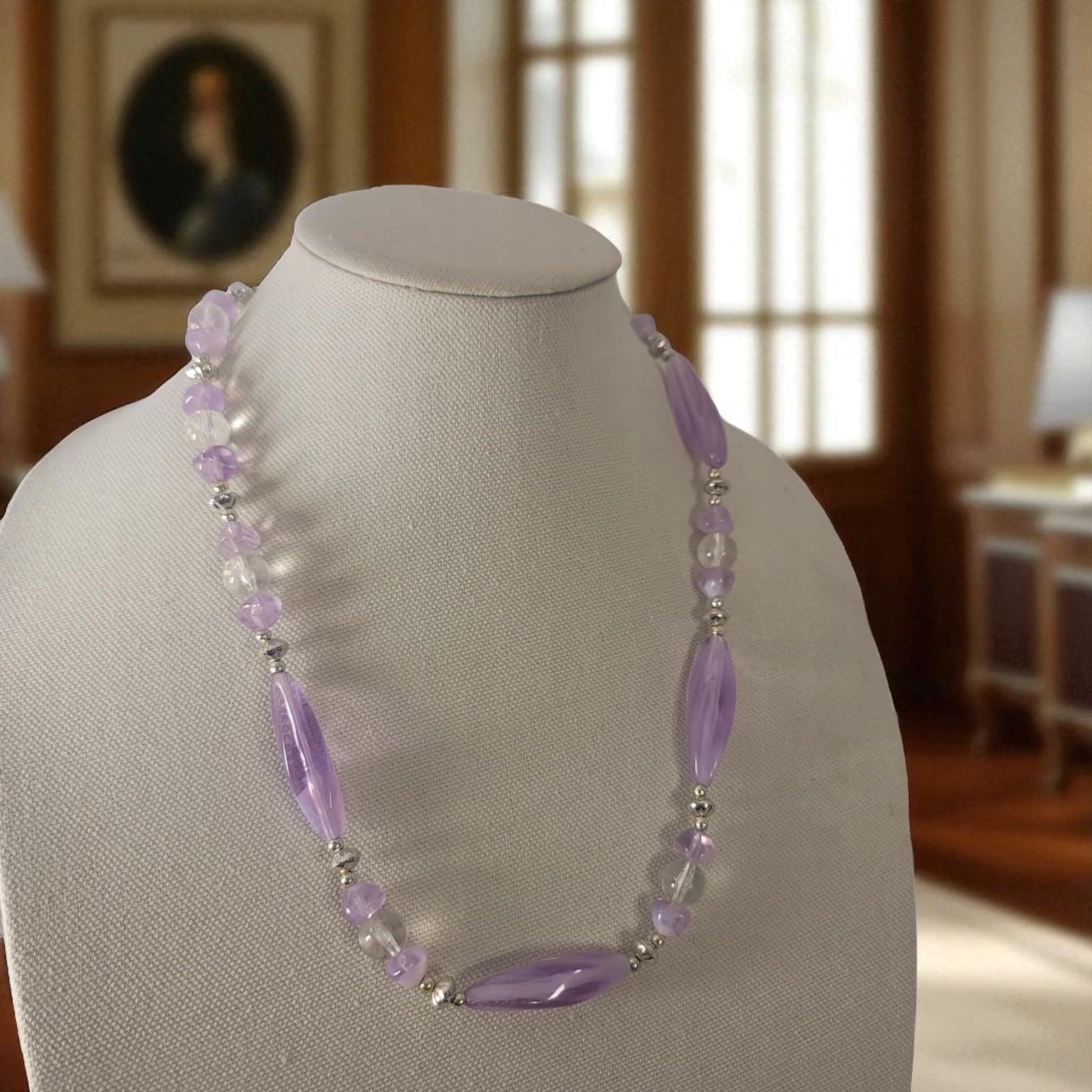 Necklace with purple and clear beads on a mannequin bust in a room setting.