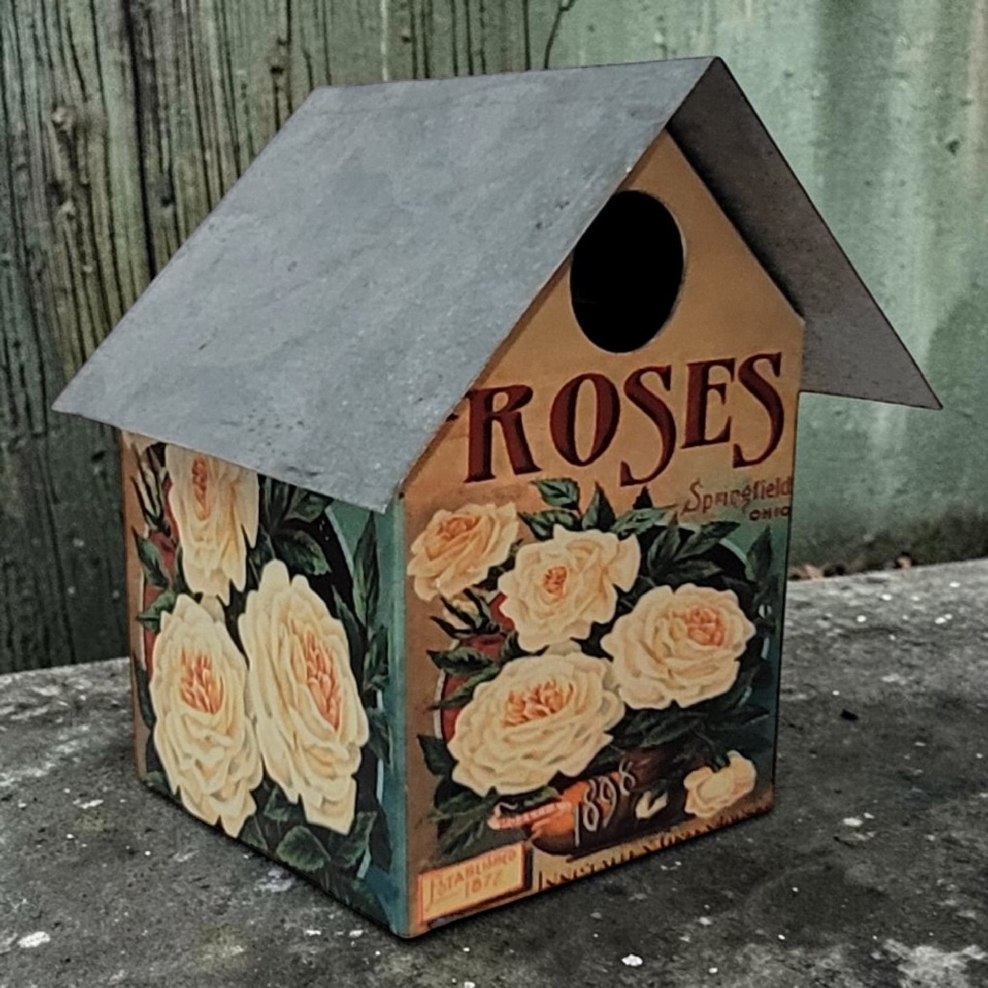Handcrafted rustic rose-themed birdhouse made from reclaimed materials for garden and outdoor décor.
