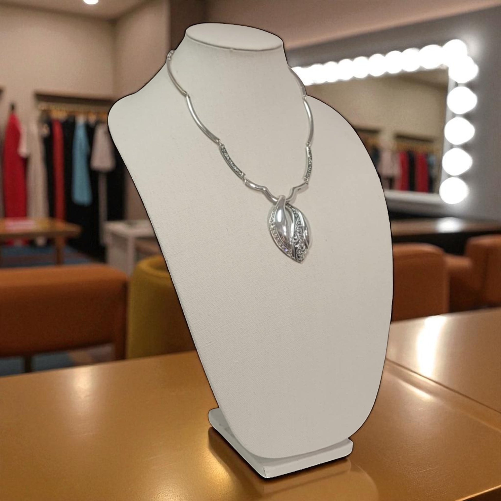Silver necklace on a white mannequin bust in a store setting with clothing racks in the background.