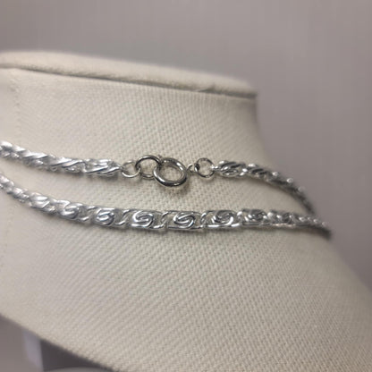 Silver chain necklace on a mannequin bust against a plain background