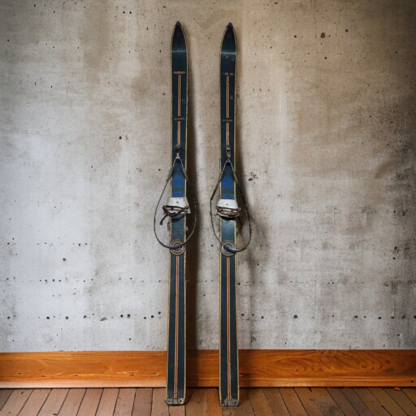 Pair of vintage skis against a textured concrete wall.
