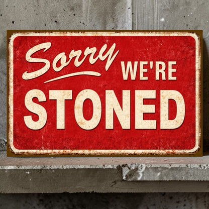Red sign with 'Sorry We're Stoned' text on a concrete wall.