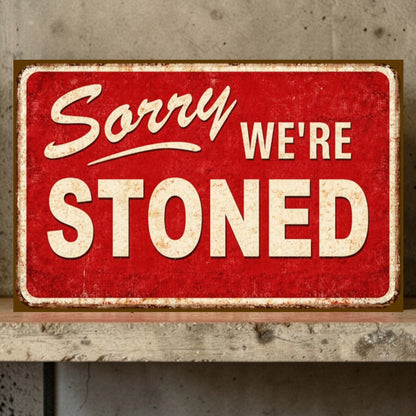 Red sign with white text 'Sorry WE'RE STONED' on a wooden surface.