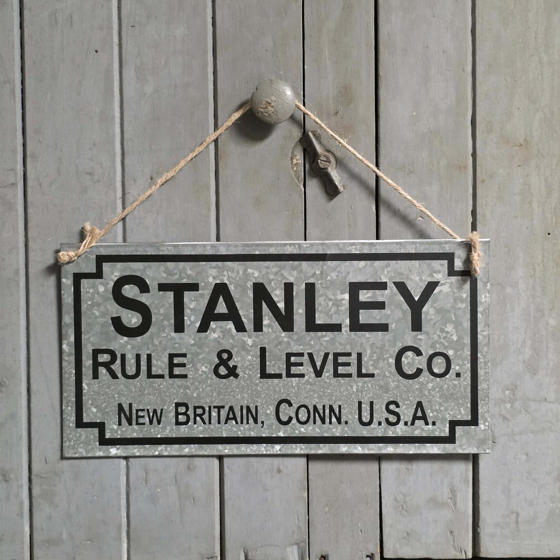 Vintage-style sign for Stanley Rule & Level Co. hanging on a wooden wall.