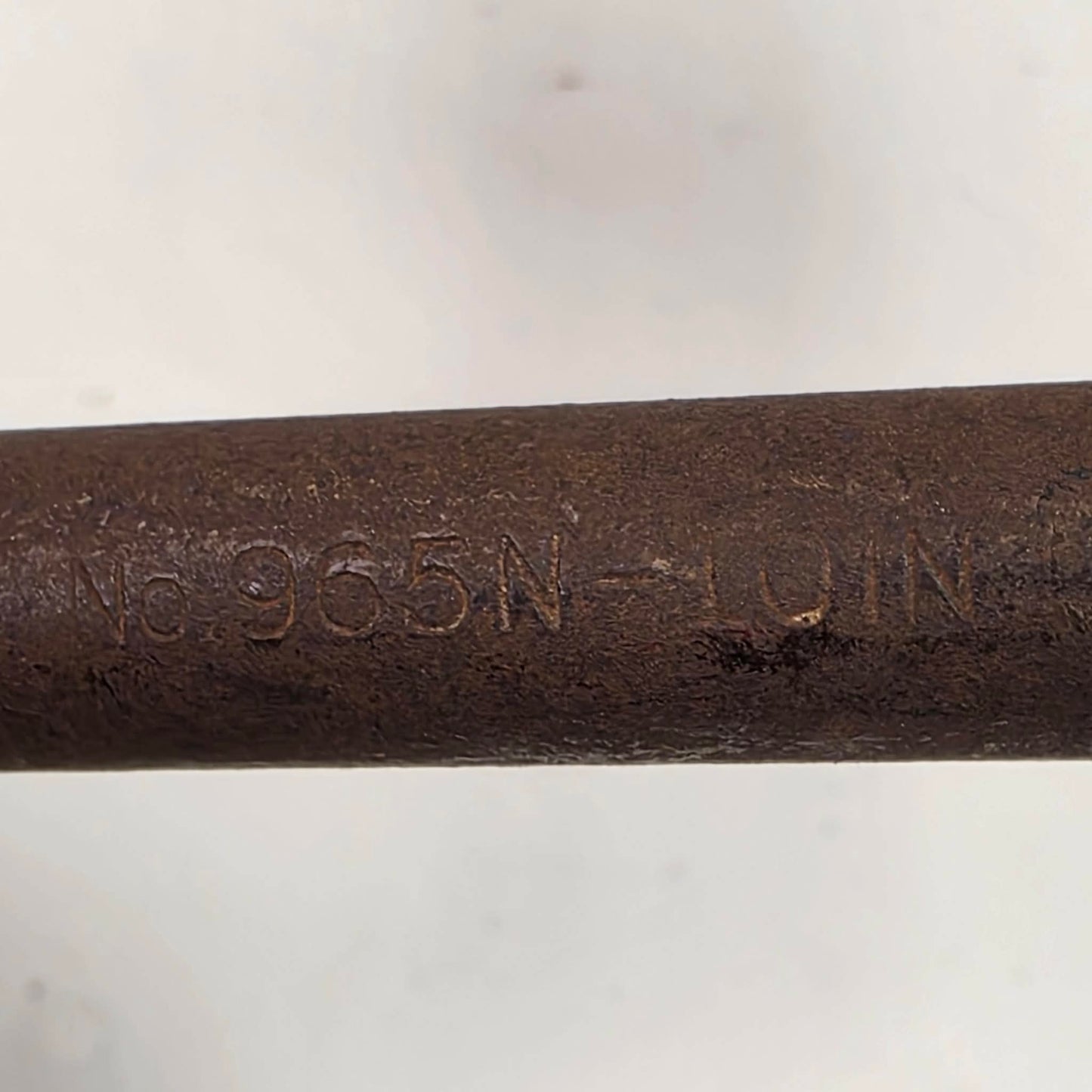 A close-up of a dark brown cast iron or steel rod stamped with the alphanumeric code 'No. 965N - LOIN' on a light gray background.
