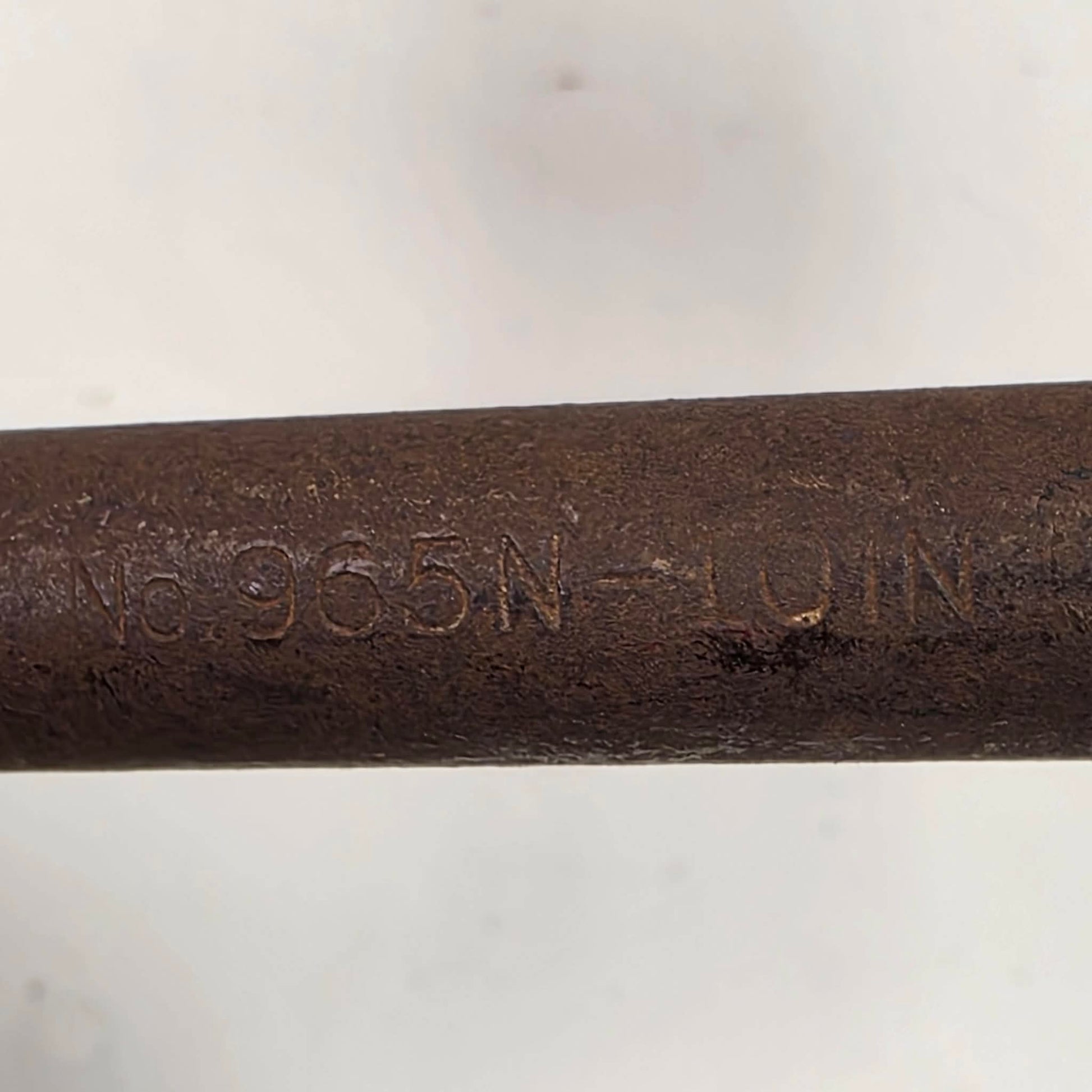 A close-up of a dark brown cast iron or steel rod stamped with the alphanumeric code 'No. 965N - LOIN' on a light gray background.