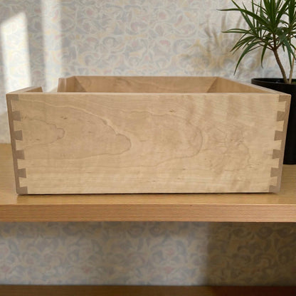 Wooden planter box on a wooden surface with a plant in the background