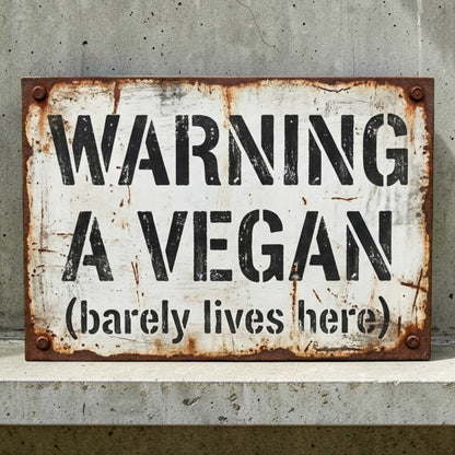 Rustic metal sign with text 'Warning: A Vegan (barely lives here)' on a concrete wall.
