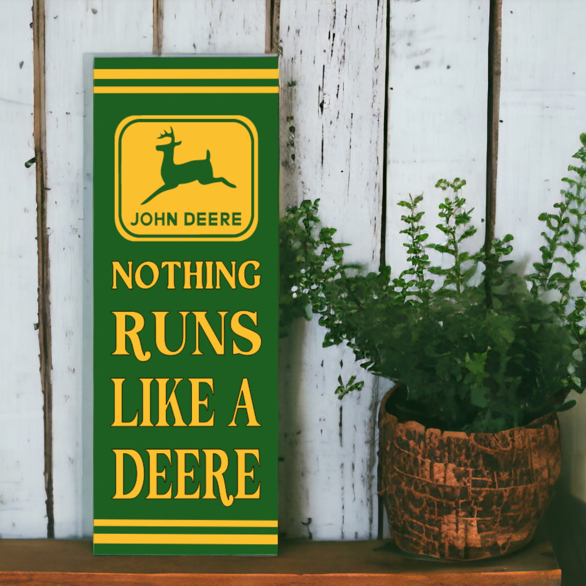 A vertical, retro style John Deere sign featuring the brand logo with the text 'NOTHING RUNS LIKE A DEERE' in bold lettering, placed against a wooden backdrop with green plants to the side.