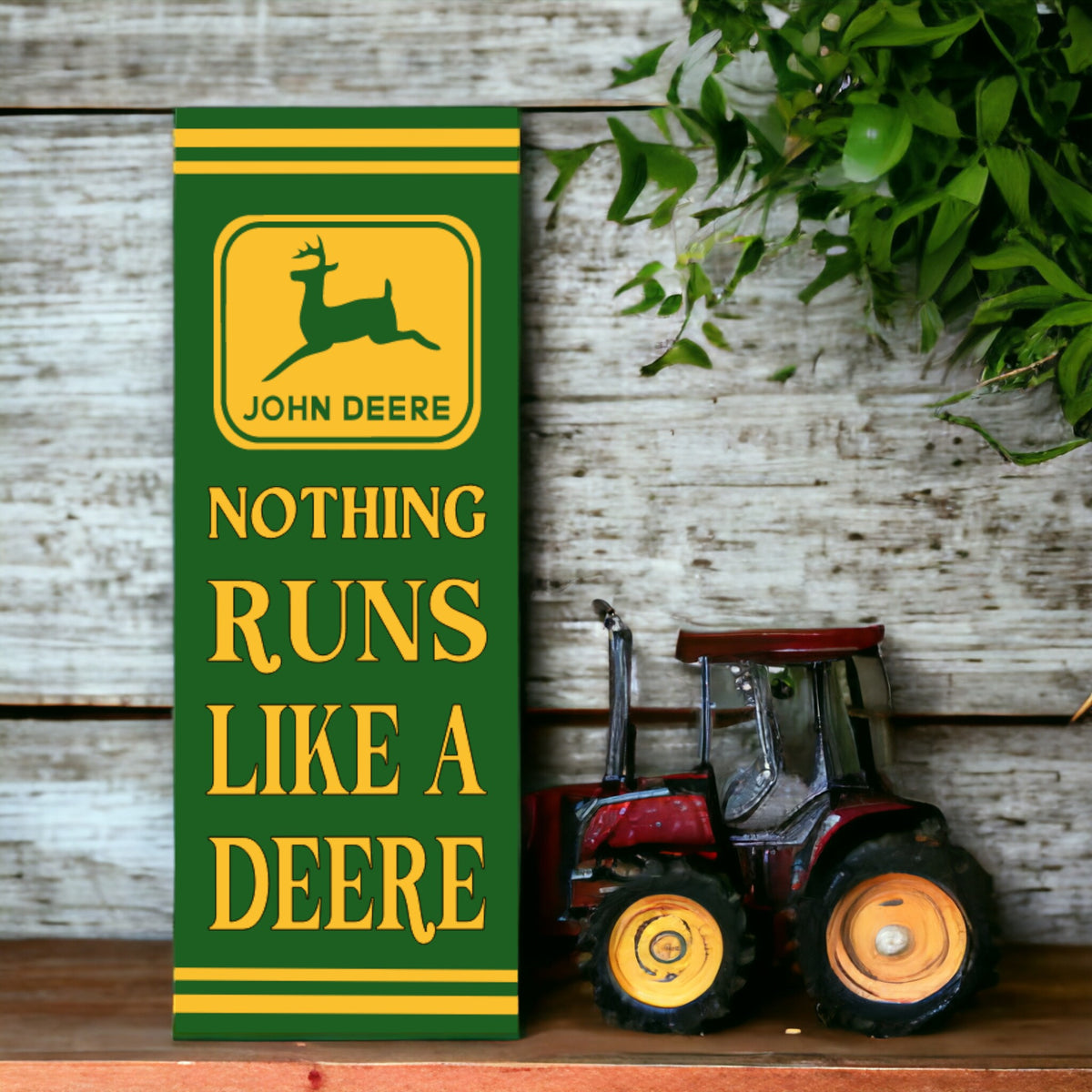 A vertical, retro style John Deere sign featuring the brand logo with the text 'NOTHING RUNS LIKE A DEERE' in bold lettering, placed against a wooden backdrop with green plants to the side.
