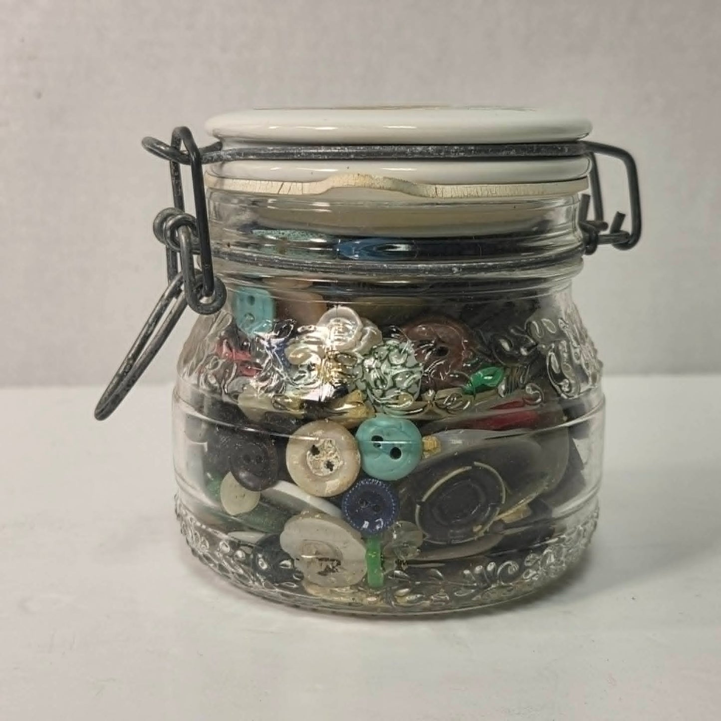 Clear glass jar filled with various buttons on a white background
