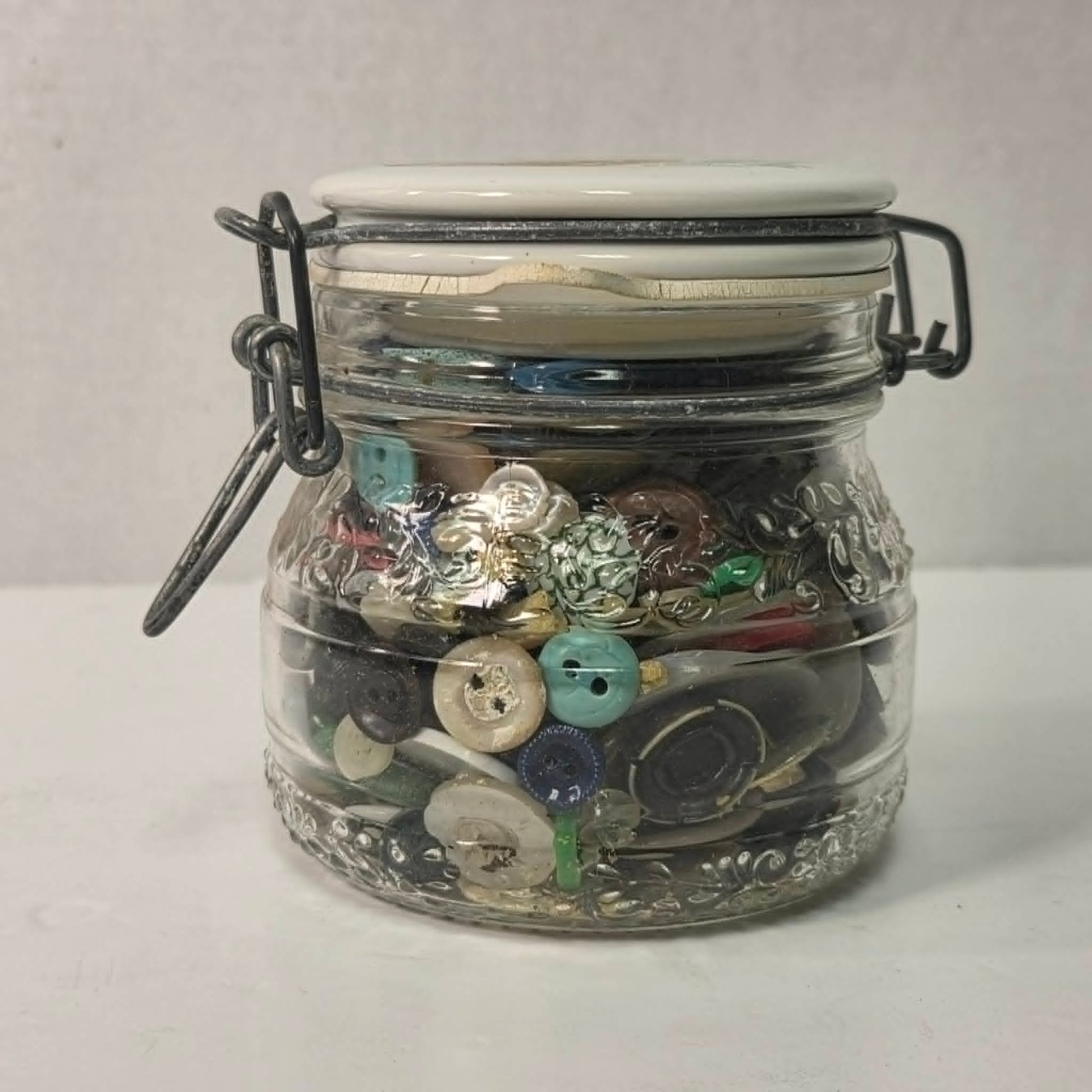 Clear glass jar filled with various buttons on a white background