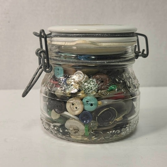 Clear glass jar filled with various buttons on a white background