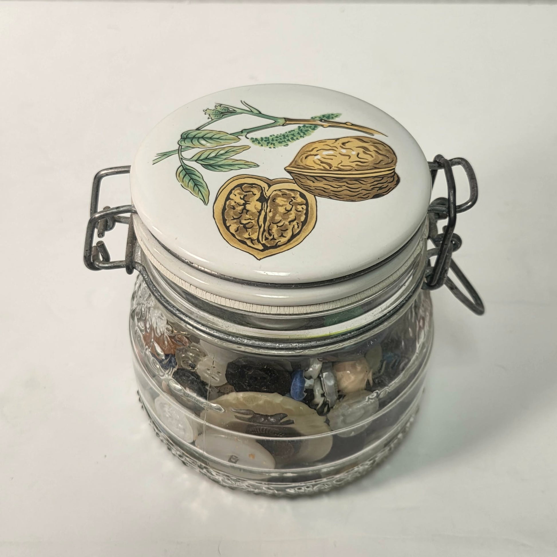 Glass jar with decorative lid featuring illustrations of walnuts on a white background
