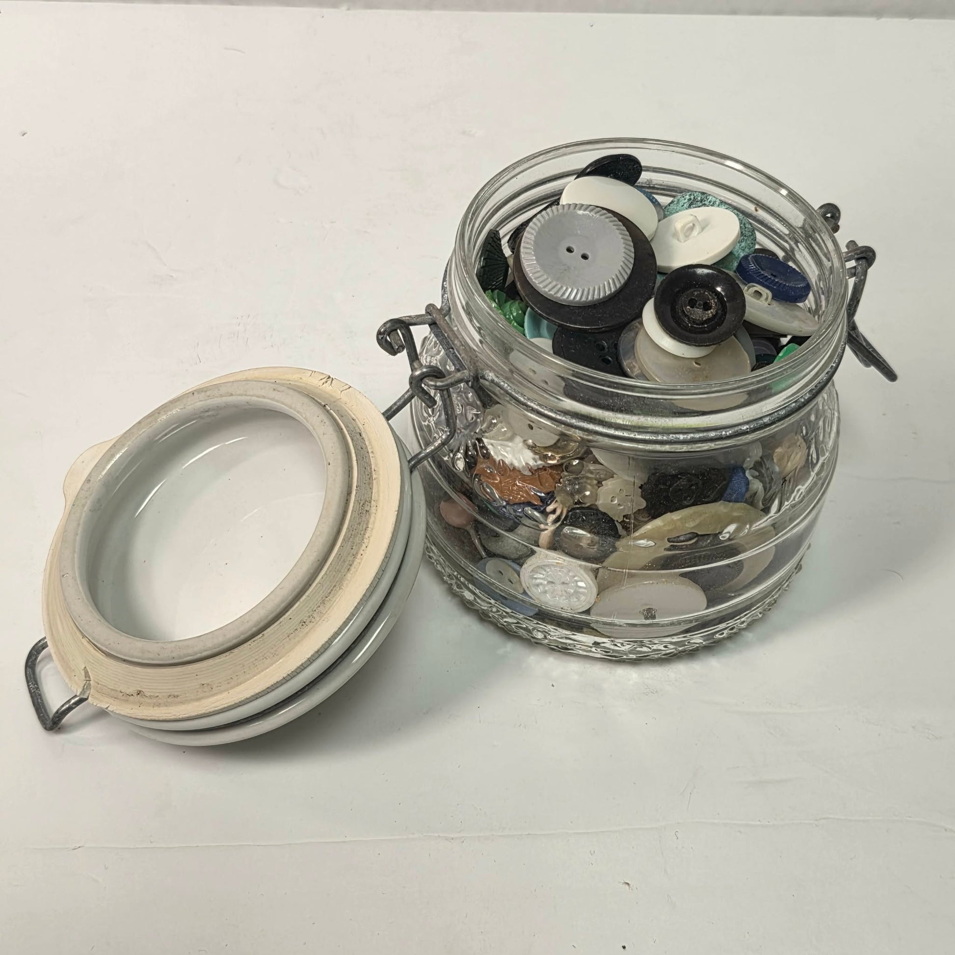 Glass jar with airtight lid filled with various buttons on a white background