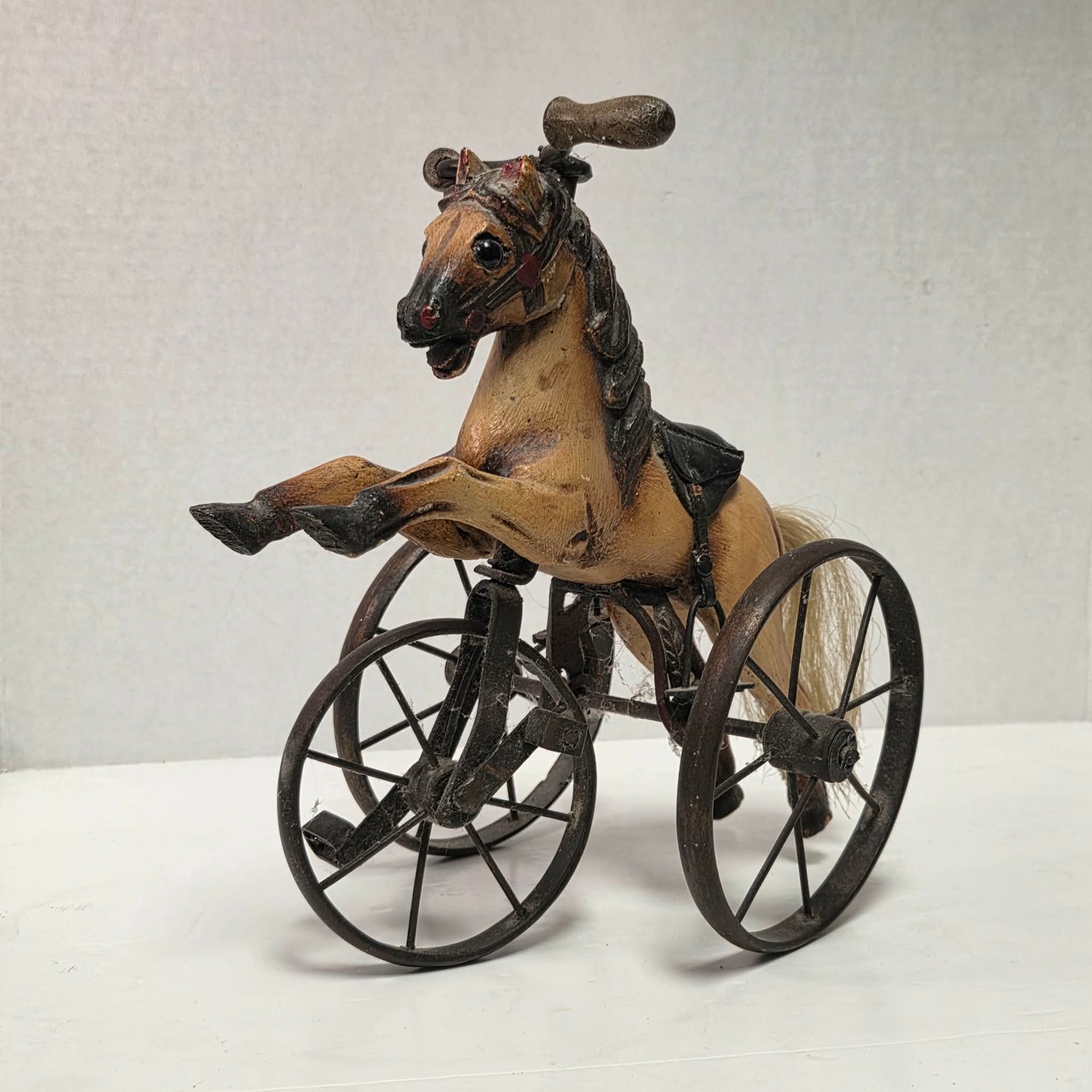 Vintage miniature wooden toy horse ride-on velocipede with carved wooden body, iron wheels, and pedals. Antique collectible toy display piece from a bygone era.
