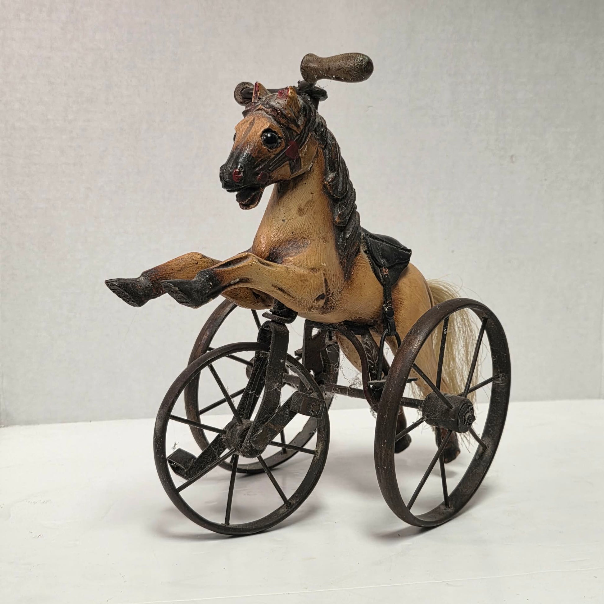 Vintage miniature wooden toy horse ride-on velocipede with carved wooden body, iron wheels, and pedals. Antique collectible toy display piece from a bygone era.