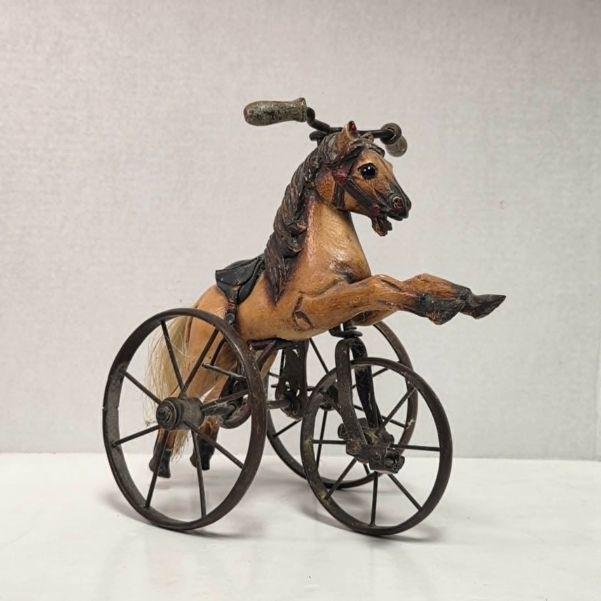 Vintage miniature wooden toy horse ride-on velocipede with carved wooden body, iron wheels, and pedals. Antique collectible toy display piece from a bygone era.