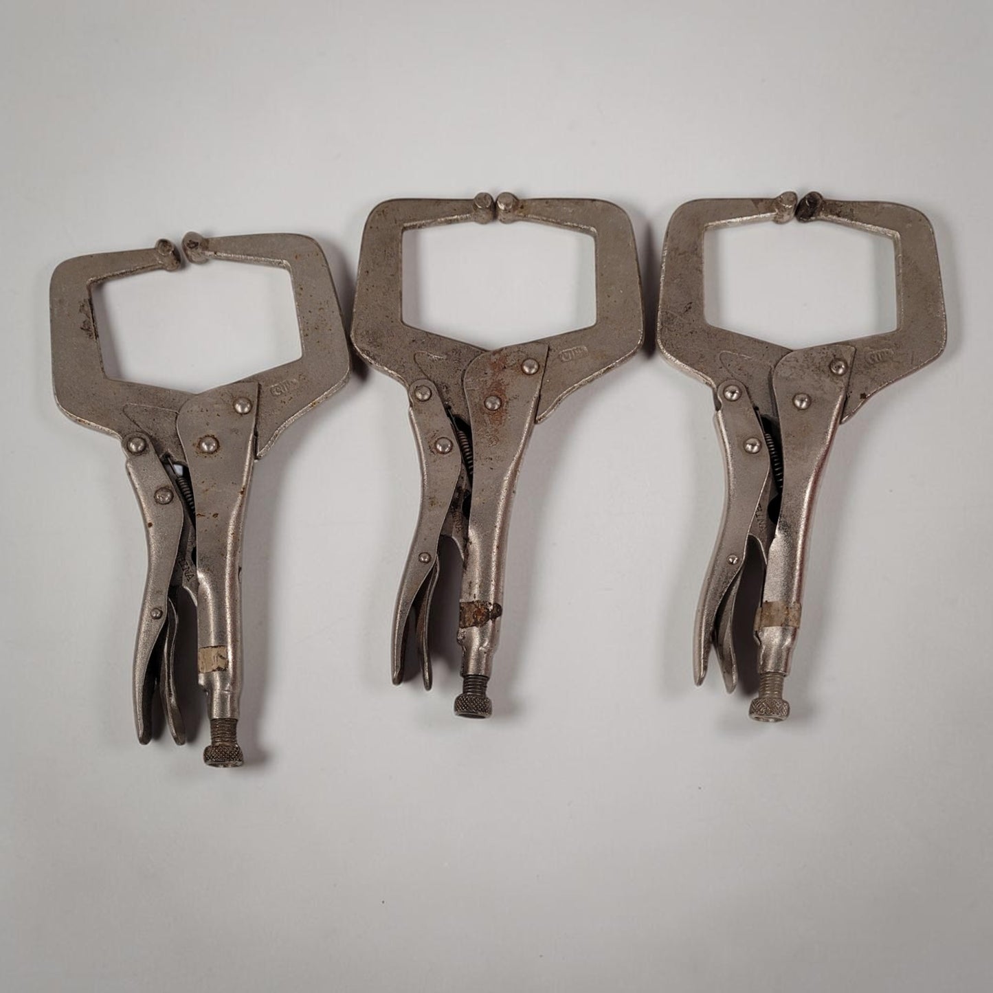 Set of three 11 inch C-clamp locking pliers used for welding and metal fabrication in a workshop setting.