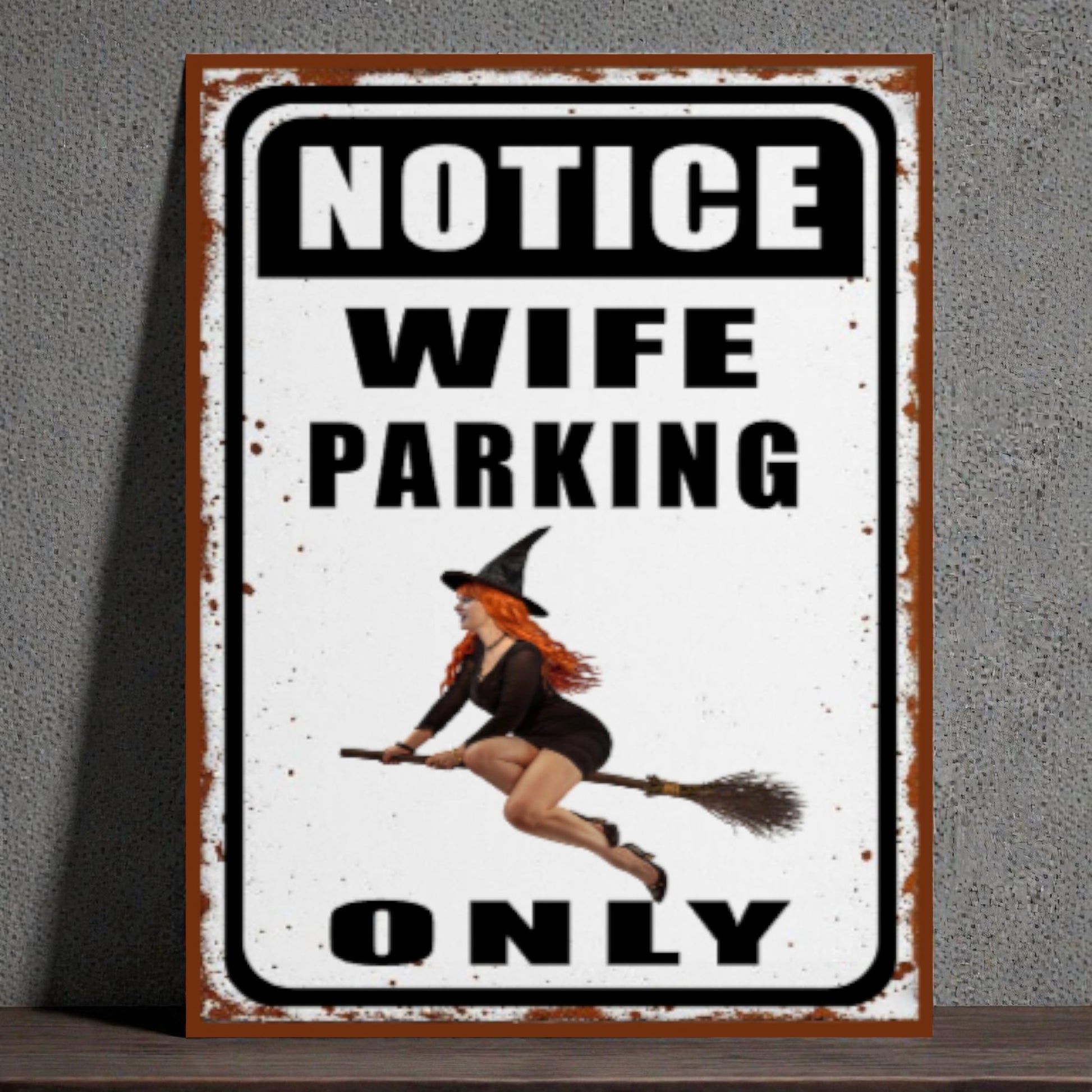 Metal sign with a witch design and text 'Notice Wife Parking Only' on a gray background