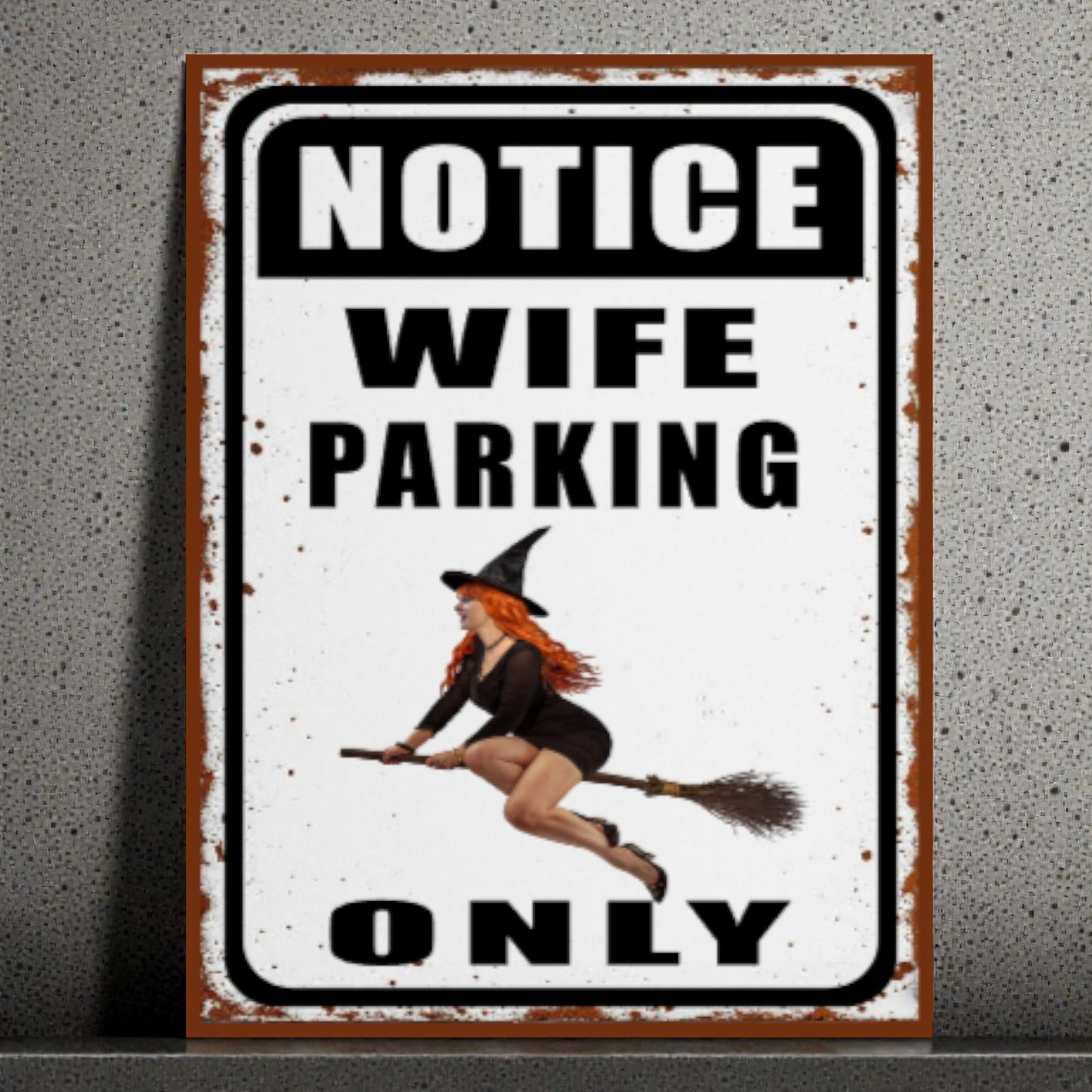 Metal sign with a witch design and text 'Notice Wife Parking Only' on a textured wall background.