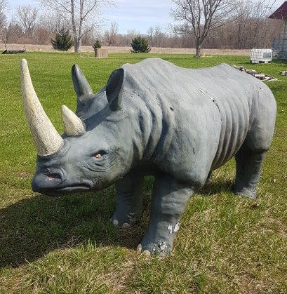 Life-size fiberglass rhinoceros statue with weathered paint, outdoor commercial display prop for theme parks or attractions.